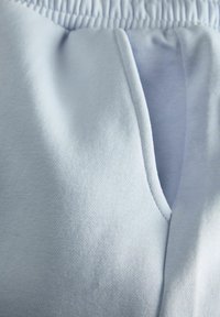 Pantalons de jogging bleu clair en tissu doux et texturé, avec une taille élastique et une fente latérale pour plus de détails.