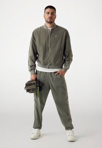 Chaqueta bomber verde oliva con puños y dobladillo acanalados, combinada con pantalones ajustados a juego. Presenta un acabado texturizado y bolsillos laterales.