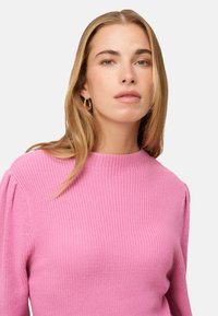 Maglione rosa lavorato a maglia con texture a coste, scollo rotondo e maniche a sbuffo morbide, con una vista ravvicinata della parte superiore del corpo.