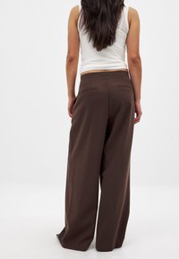 Pantalones de pierna ancha marrones con una textura suave, que cuentan con dos bolsillos traseros y una cintura alta, combinados con una camiseta sin mangas blanca ajustada.