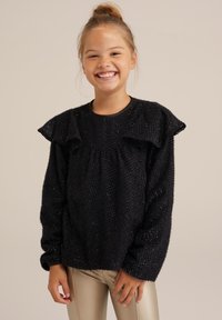 Črn pulover z teksturo in volanastimi rokavi ter okroglo ovratnikom. Obut nad sijočimi zlatimi legginsom. Soft, puhov material z rahlim leskom.