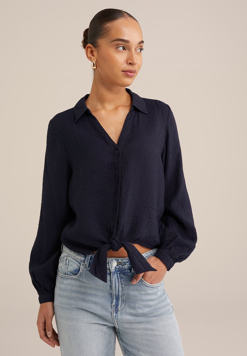 Kara jūras zilas, vieglas pogās aizdara krekli, ar garām piedurknēm un jostu viduklī. Strukturēts audums ar brīvu piegriezumu, apvienots ar gaiši zilām džinsām.