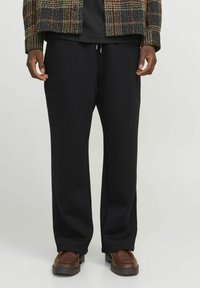 Pantaloni sportivi negri, cu un croi lejer, realizați dintr-un material moale și neted, cu talie elastică și detaliu cu șnur. Nu au modele vizibile.