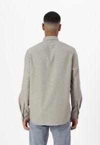 Camisa de manga larga gris claro con cuello abotonado, detalles en el yugo trasero y puños, hecha de una tela texturizada. Combinado con jeans azul claro.