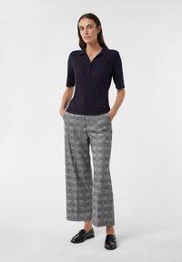 Granatowa polo z krótkim rękawem w prążki, zestawiona z szerokimi, szarymi spodniami w kratkę oraz czarnymi mokasynami. Gładka tekstura, swobodny krój.