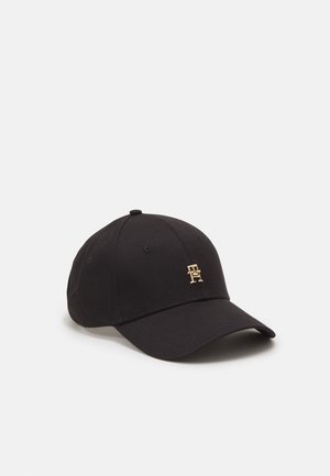 Black baseball cap with curved brim and small gold logo featuring interlocked letters on the front panel, on a plain light background.
