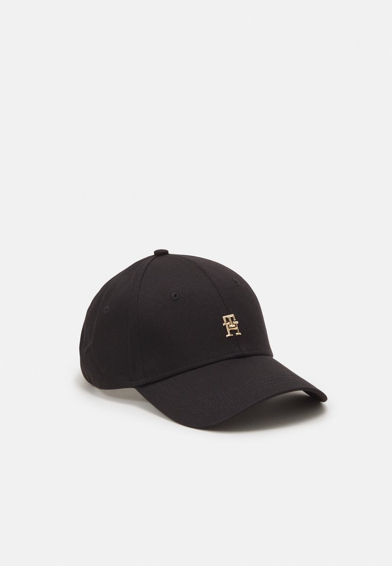Casquette de baseball noire avec une visière incurvée et un petit logo doré présentant des lettres entrelacées sur le panneau avant, sur un fond clair uni.