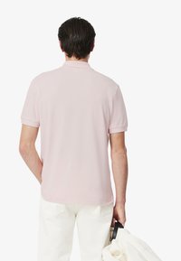 Ljusrosa kortärmad polo med en slät textur, platt krage och diskreta sömmar, kombinerad med vita byxor och en väska.