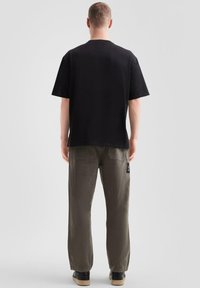 Czarny t-shirt z krótkim rękawem zestawiony z jasnoszarymi, luźnymi spodniami, które mają tylne kieszenie i metkę z logo, noszony z czarnymi butami.
