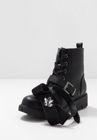 Bottes noires en cuir à lacets avec une boucle sur le côté, assorties à un accessoire capillaire en velours noir en forme de nœud orné de cristaux transparents.