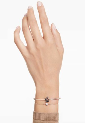 Roségoldfarbener Manschettenarmreif mit Schwan-Design, schwarzen Akzenten und einem kleinen klaren Stein, getragen an einer Hand mit heller Haut.