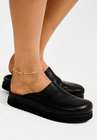 Mustad nahast klotskingad laiade avatud detailide ja massiivse musta tallaga. Materjalil on peen sära ja kergelt nähtav tekstuur.