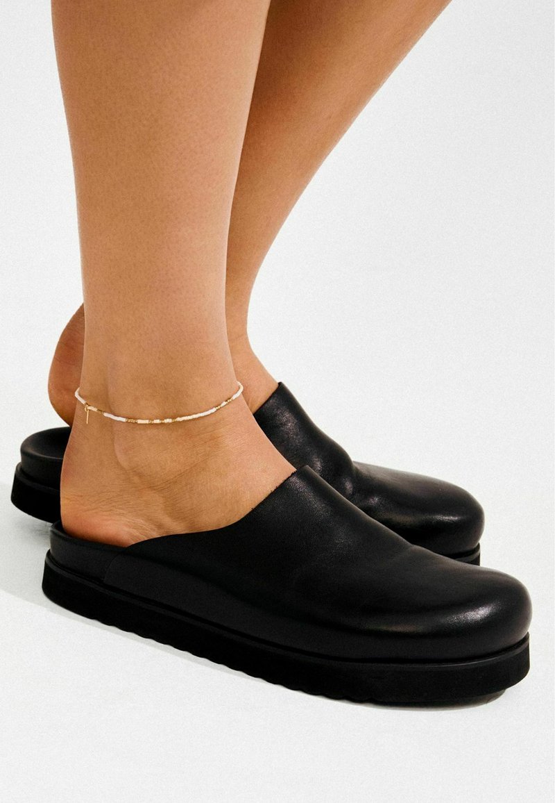 Mustad nahast klotskingad laiade avatud detailide ja massiivse musta tallaga. Materjalil on peen sära ja kergelt nähtav tekstuur.