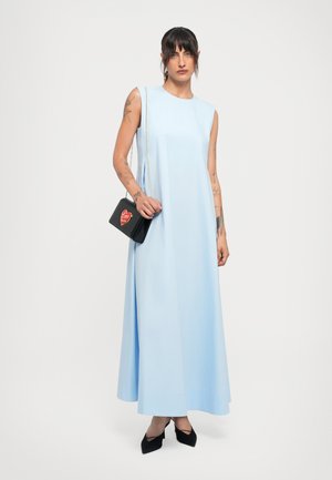 Woman with tattoos wearing a sleeveless light blue maxi dress, holding a black purse with a red heart and the word "Love."