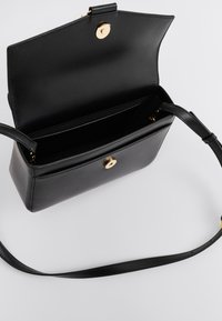 Μαύρη δερμάτινη τσάντα με επίπεδο σχέδιο, μεταλλικό χρυσό κουμπί και μακρύ ρυθμιζόμενο λουρί. Το εσωτερικό είναι επενδεδυμένο και ευρύχωρο, με θήκη για πιστωτικές κάρτες.