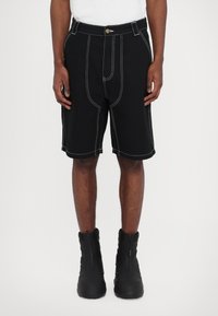 Black shorts with contrast white stitching, featuring a button closure, angled side pockets, and a relaxed fit, paired with black zip boots.
