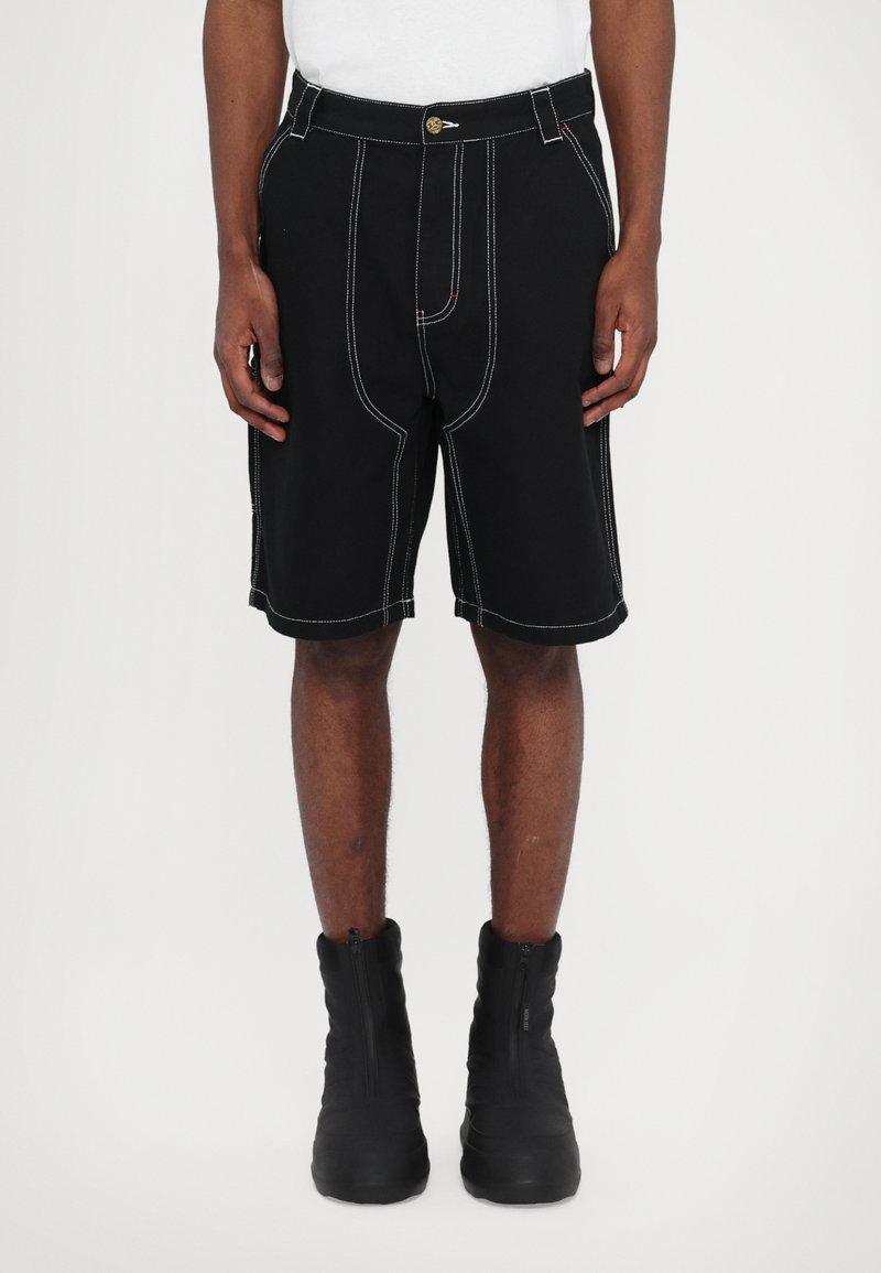 Black shorts with contrast white stitching, featuring a button closure, angled side pockets, and a relaxed fit, paired with black zip boots.