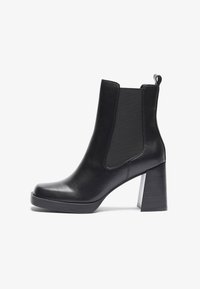 Bottines en cuir noir avec un talon épais, des panneaux latéraux élastiques et une languette à l'arrière. Texture lisse et forme de bout arrondi.