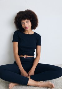 Navy short-sleeve T-shirt with a knotted front, paired with matching high-waisted leggings featuring a small logo. Soft, stretchy fabric.