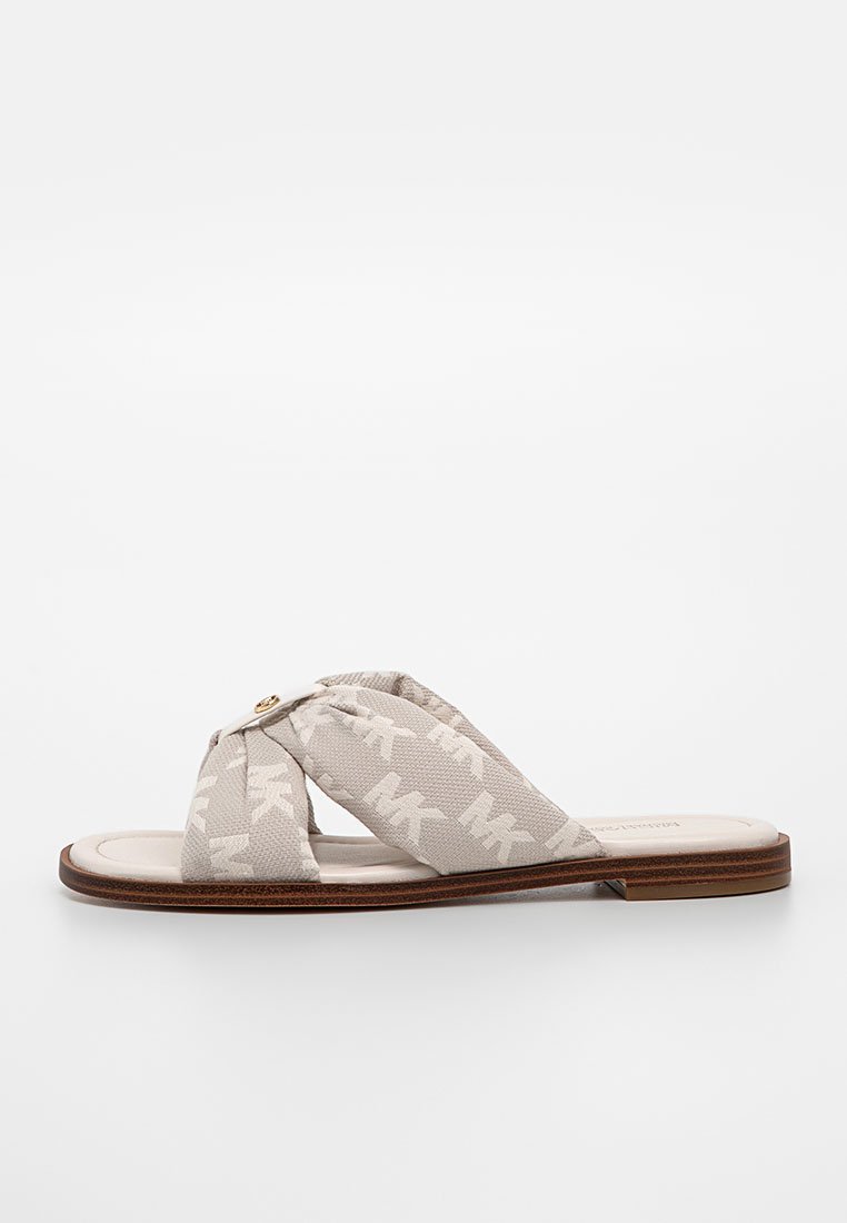 Sandale à glisser en tissu beige avec des brides croisées se chevauchant, présentant un motif subtil "MK", un bouton doré en accent et une semelle plate marron.