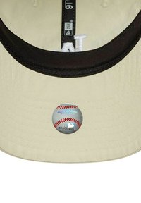 Baseballkappe aus beigem Stoff, schwarzem Schirm und einem runden Aufkleber mit einem Baseball-Motiv auf der Innenseite.