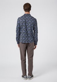 Langarmshirt in donkerblauw met bloemenpatroon, gecombineerd met lichtbruine, getextureerde broeken en grijze sneakers met donkere accenten.