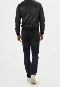 Giubbotto bomber in pelle nera con polsini e fondo a coste, abbinato a jeans scuri e sneaker bianche, visto da dietro.