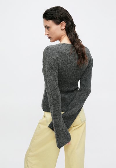 Pulover gri, mulat, cu mâneci lungi și textură ușor striată, purtat cu pantaloni galbeni deschiși. Material moale, design simplu.