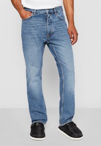Light blue straight-leg jeans made of denim, featuring a classic five-pocket design, stitched accents, and a button fly closure.
