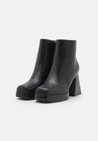 Botas negras hasta el tobillo de cuero suave, con un tacón grueso y suela de plataforma. Detalle de cremallera en la parte trasera, líneas limpias y punta redondeada.
