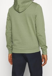 Felpa verde realizzata in morbido tessuto, con un ampio cappuccio, polsini e orlo a costine. Il retro presenta una texture liscia senza loghi visibili.