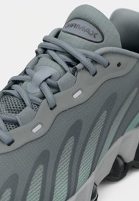 Gray athletic shoe with textured mesh and smooth overlays. Features a distinctive wavy design and rubber outsole with visible air cushioning.