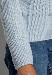Ljust blå stickad tröja med ribbad struktur och långa ärmar, matchad med denim. Tyget verkar mjukt och bekvämt.