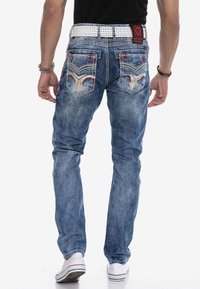Blaue Jeans aus Denim mit schmaler Passform, versehen mit bestickten Gesäßtaschen, kontrastierendem roten Nähten und einem weißen Gürtel.