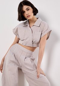 Camisa cortada de rayas en marrón claro y blanco con mangas cortas y detalles de bolsillo; pantalones de pierna ancha a juego con plisados en la cintura.