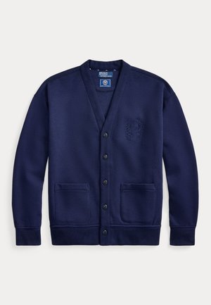 Mørkeblå cardigan med knapper foran, to lommer foran og broderet våbenskjold på brystet, lange ærmer samt ribstrikkede manchetter og kant.