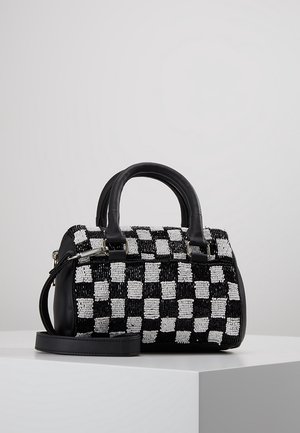 Sac à main à carreaux noir et blanc avec texture perlée, poignées en cuir noir et bandoulière amovible, posé sur une surface blanche.
