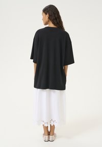 Sort oversized t-shirt lavet af blødt stof, parret med en hvid, ankel-lang nederdel med bølgede blonder langs kanten.