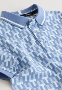 Polo bleu clair à manches courtes avec motif géométrique blanc et bleu plus foncé et texte "BAKER", avec col côtelé et patte de boutonnage à trois boutons.