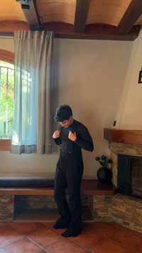 Zwarte top met lange mouwen en broek, met bretels. Aansluitend ontwerp met een gladde textuur. Staand in een goed verlichte kamer met natuurlijke elementen.