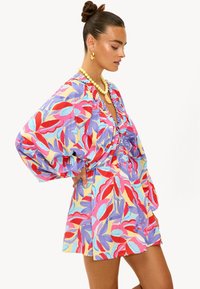 Robe colorée à motifs présentant de grands motifs floraux en rouge, violet et bleu. Fabriquée en tissu léger avec des manches bouffantes et une taille cintrée.