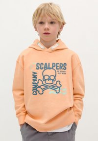 Ljusorange hoodie med en grafisk design av ett skalle och korsade ben, dragsko på huvan och ribbade ärmslut. Tillverkad av bomull, avslappnad passform.