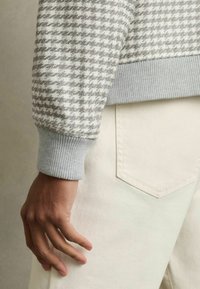 Jersey de punto a rayas en gris y blanco con puños gris de canalé, combinado con pantalones blancos que cuentan con un bolsillo trasero.