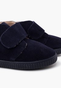 Par de zapatos infantiles de ante azul marino con suelas de goma negra texturizada y amplias correas de velcro para el cierre.