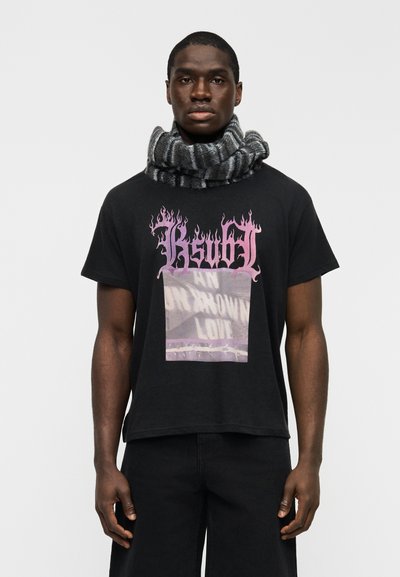 T-shirt en coton noir avec des motifs de flammes roses et un portrait imprimé. Écharpe rayée grise et noire enroulée autour du cou.