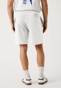 Pantalones cortos de algodón blancos con un corte relajado, que cuentan con un bolsillo trasero y el logo "PEPE JEANS" por encima de la cinturilla. Combinados con zapatillas blancas.
