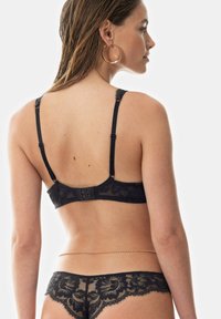 Reggiseno in pizzo nero e slip coordinato mostrati da dietro. Caratterizzato da motivi floreali, spalline regolabili e chiusura a gancio e occhiello.