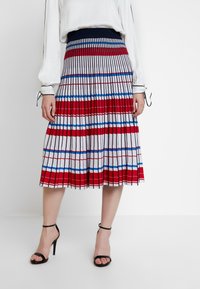 Plissé midi-rok met rood-wit-blauwe strepen. Heeft een aansluitende tailleband en een vloeiend ontwerp. Gecombineerd met zwarte sandalen met hoge hak.