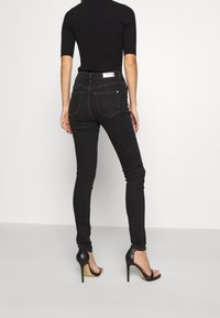 Jeans ajustados negros con cintura alta, con bolsillos traseros y costuras sutiles. Combinados con sandalias negras de tacón alto.