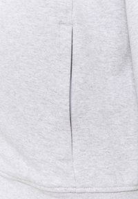 Ljust grå sweatpants med en slät textur, sidficka med en dold dragkedja och förstärkt sömnad längs sömmarna.